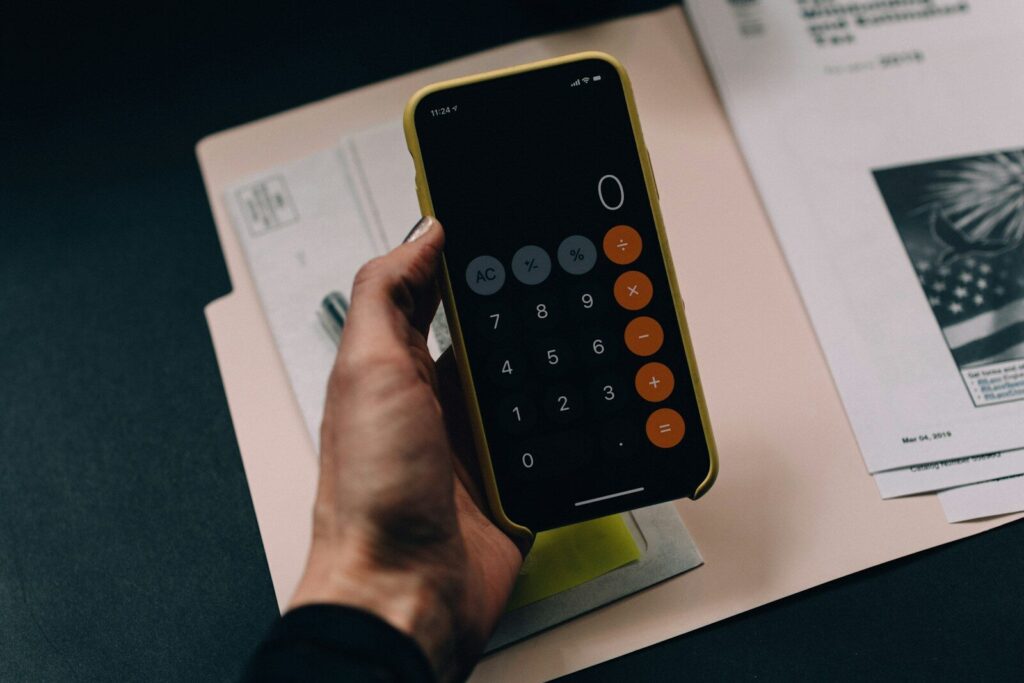 A hand holding a smartphone displaying a calculator app over a paper folder